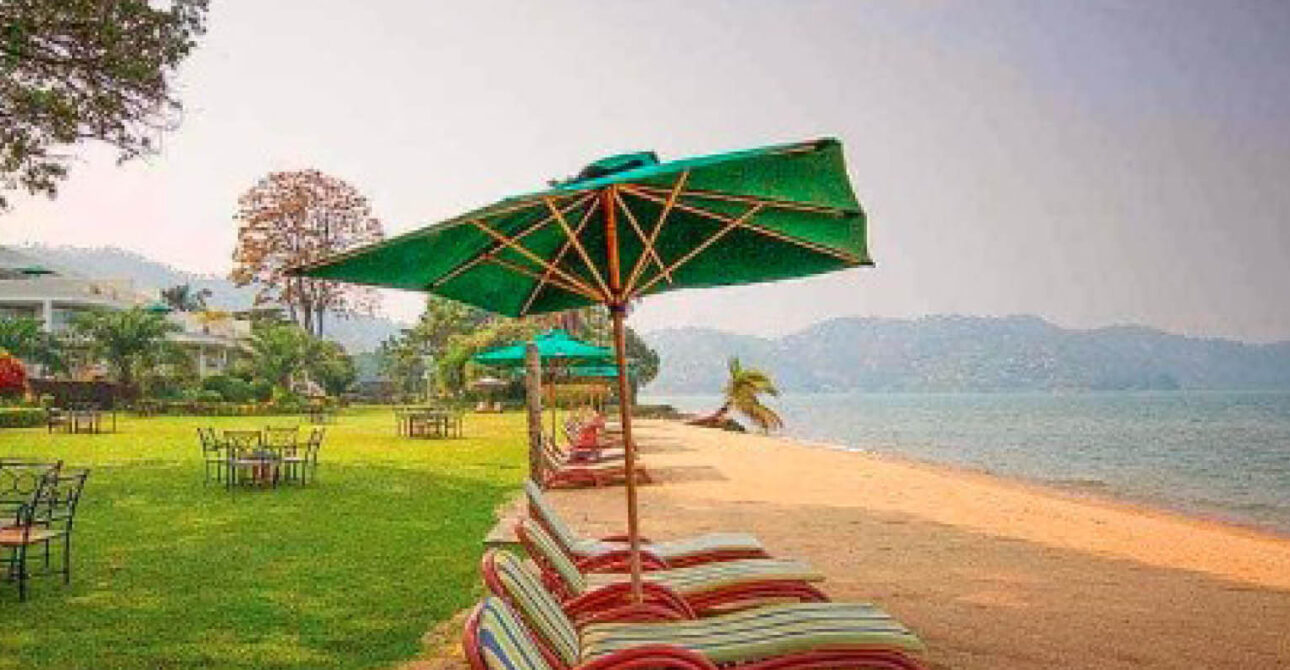 Lakeside beach at Lake Kivu in Rwanda, with shaded sun loungers, green lawns and views across the water.