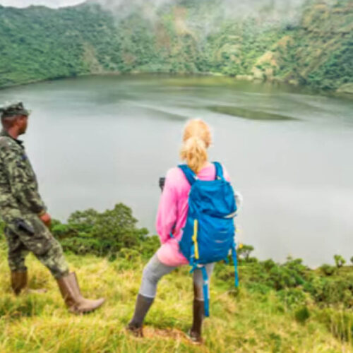 Visitor and guide overlooking a volcanic crater lake during a volcano hiking adventure in Uganda’s Virunga Mountains