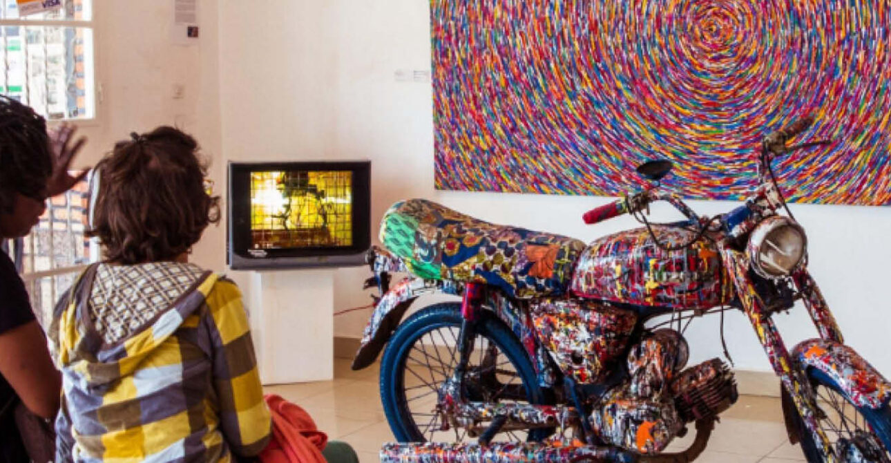 Visitors viewing colourful contemporary artwork and a decorated motorcycle inside an art gallery in Kigali, Rwanda.