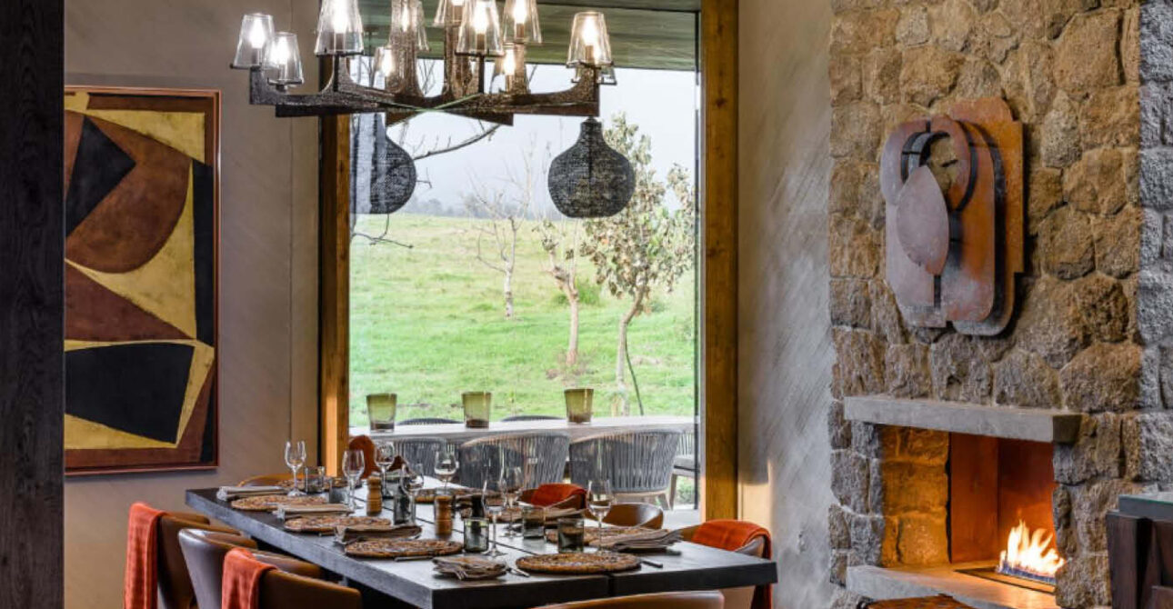 Elegant Signature safari lodge dining room featuring a beautifully arranged table, stone fireplace and scenic countryside views.