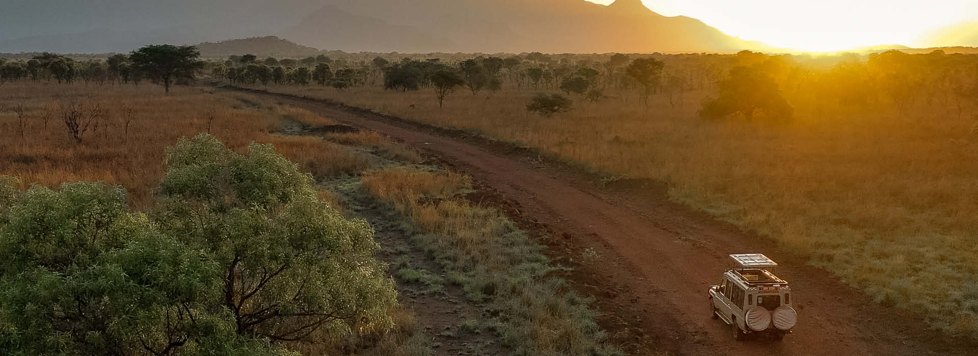 Uganda & Rwanda Safaris with a safari vehicle crossing a savannah beneath mountains at sunset