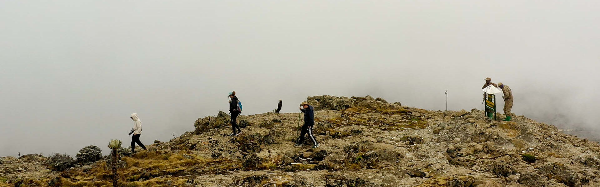 Hikers exploring a rocky mountain trail in misty conditions, illustrating adventure experiences in Uganda safari planning.