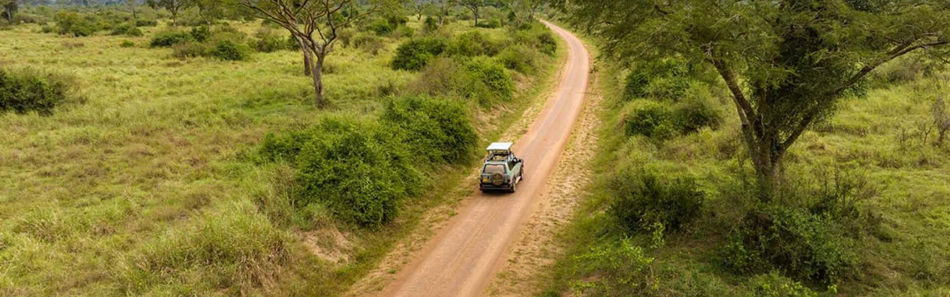 Private safari vehicle travelling along a winding road through Uganda's green savannah landscape