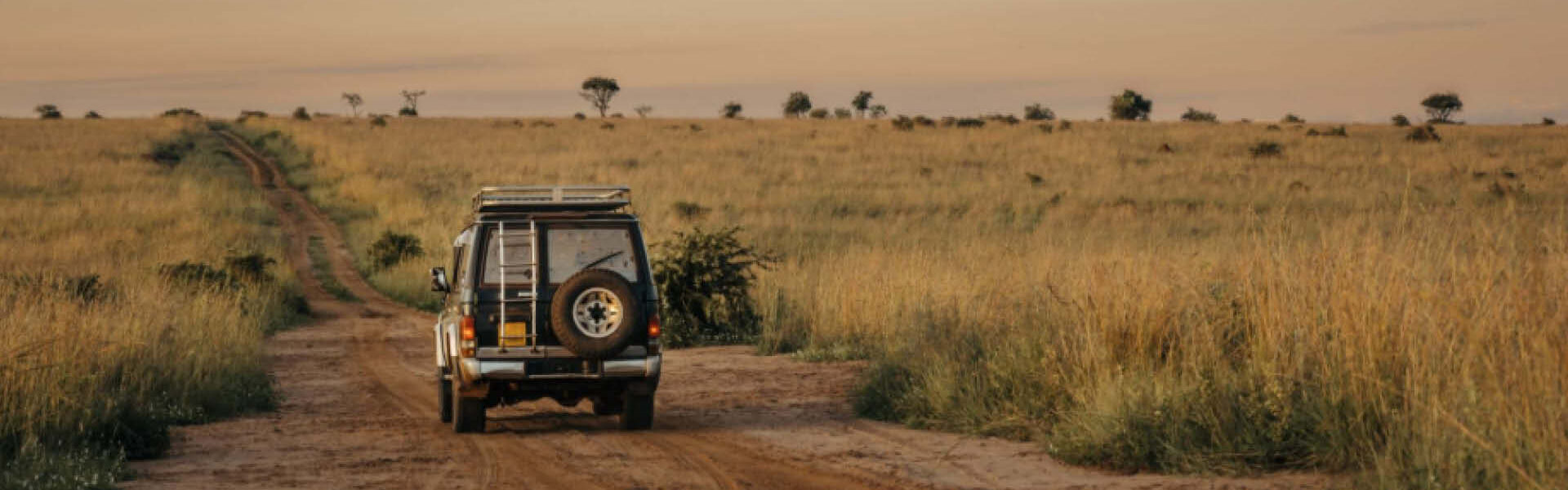 Safari vehicle travelling along a dirt track through open savannah grassland during a private wildlife safari